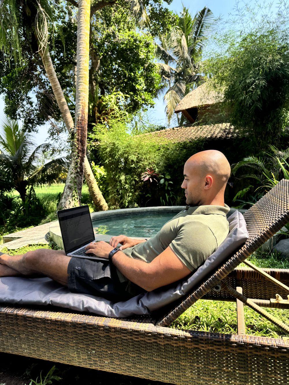 Arbeiten mit dem Laptop am Pool unter Palmen