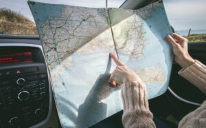 Eine Frauenhand, die im Auto auf eine Landkarte zeigt, um die besten Travel Hacks zu finden.